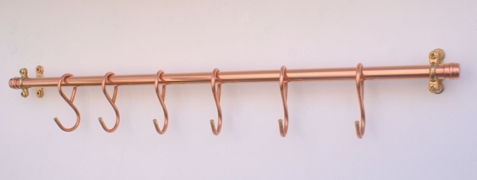 Copper pot rail with six hand-forged French hooks in rustic kitchen
